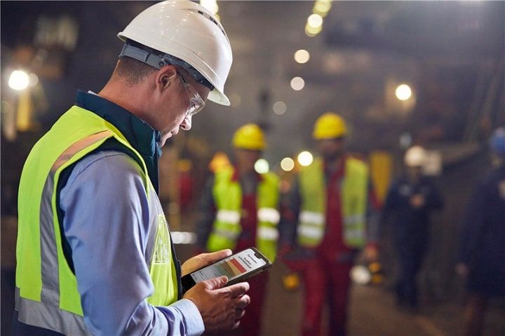 Byggarbetare med skyddshjälm tittar på mobiltelefon i en industrimiljö.